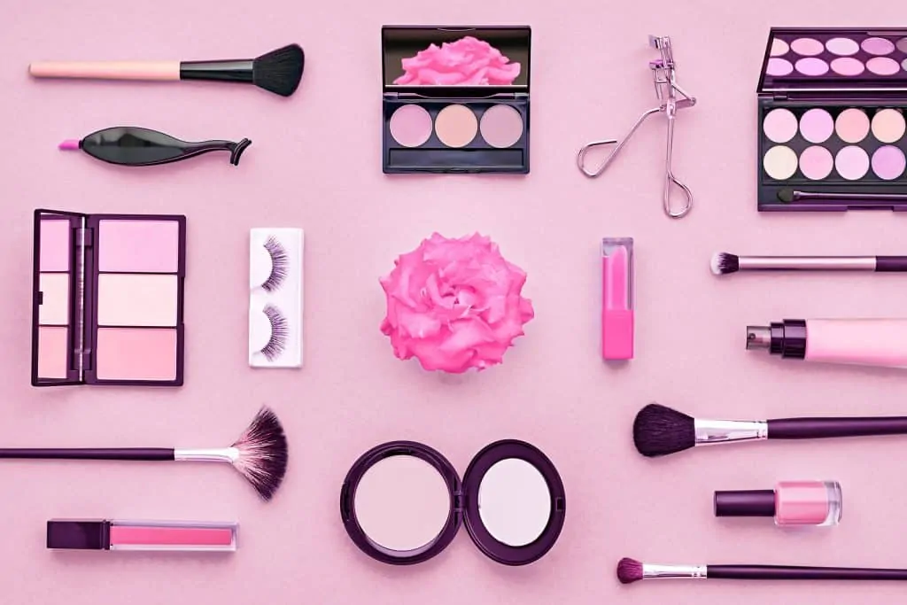 Various kinds of womens makeup on a pink table with a flower in the center