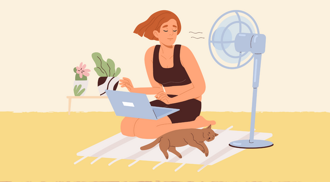 A girl using her laptop seated on the floor with a fan and a cat beside her