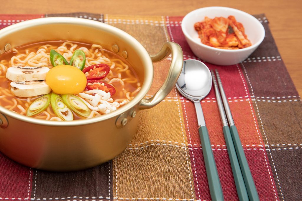 Korean Style Instant Noodle, Ramyeon With Egg Yolk and Kimchi with spoon and chopsticks on the side