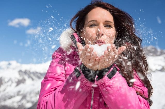 Beautiful young woman blowing snow from her hands in winter.