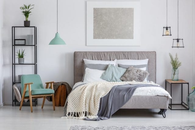 Bedroom with white walls, bed, teal chair, hanging lamps, large headboard bed, and side table