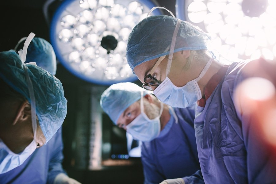 three surgeons working on a patient with lights in the background
