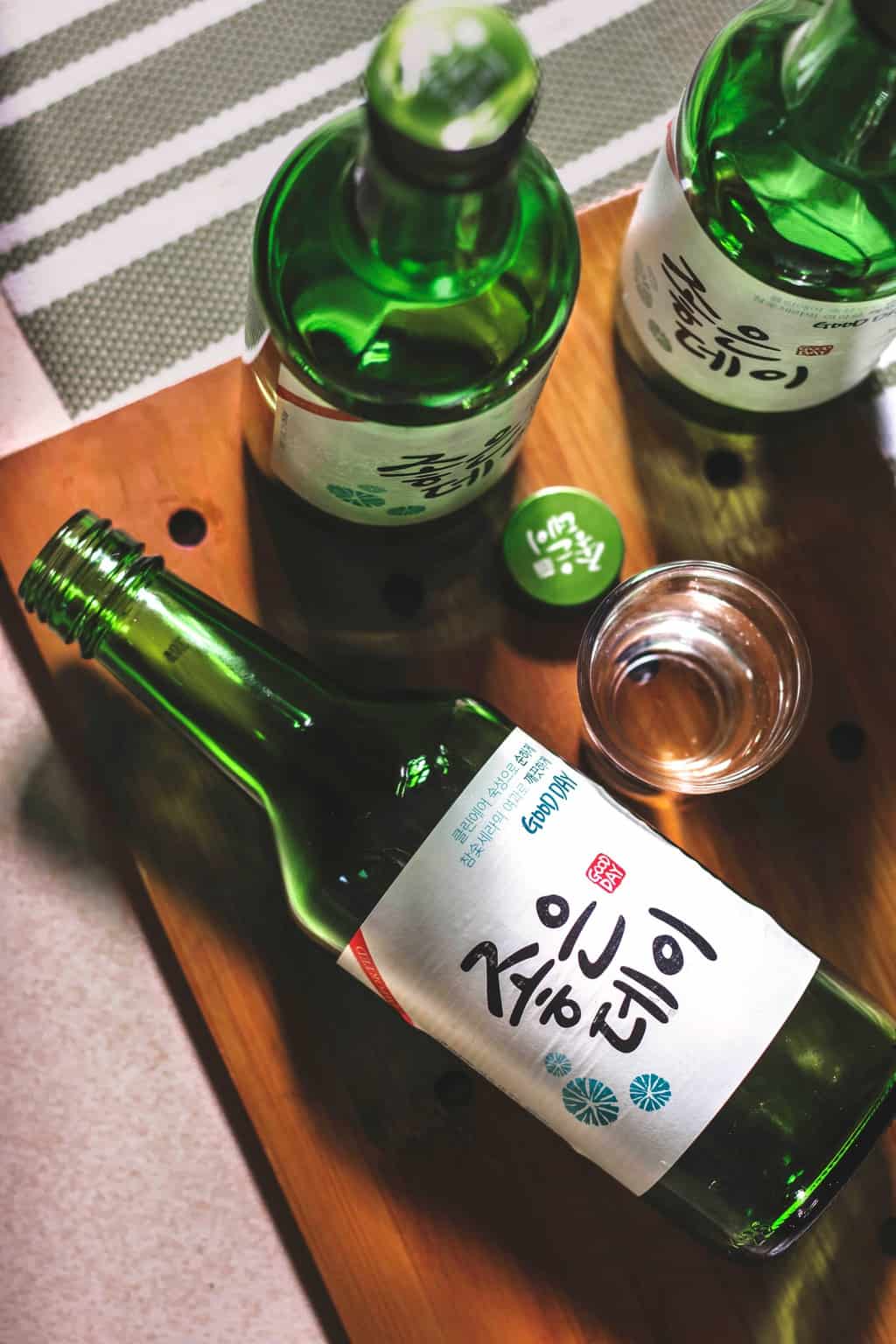 3 bottles of soju, one lying down on its side, with a soju glass near it