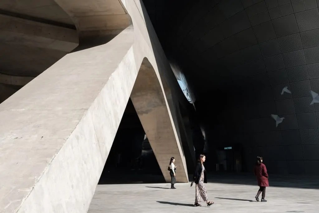 3 women walking around near a large concrete structure